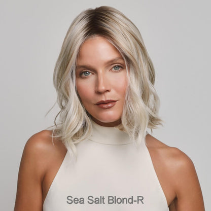 Yui  by Noriko wig in Sea Salt Blond-R. A shoulder-length wavy hair in a sea salt blonde color, wearing a cream-colored high-neck top against a light gray background. The text 'Sea Salt Blond-R' is printed at the bottom of the image.